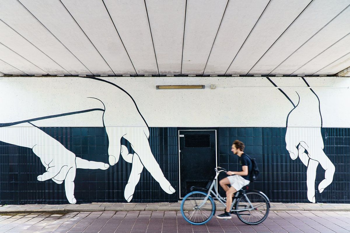 Fietser rijdt langs de muurschildering Walking Hands bij Neckerspoel in Eindhoven, met grote witte handen op een donkere wand.