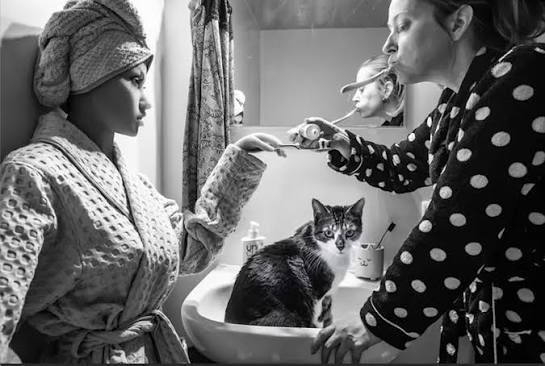 Hanneke Wetzer en de pop Nadiah in een geënsceneerde badkamerscène uit Living Alone (Together), met een kat op de voorgrond.