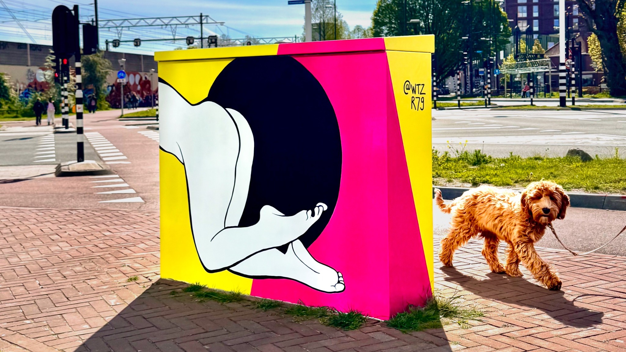 Beschilderd verkeerskastje van Hanneke Wetzer in Eindhoven met een zwart-witte figuur op een felgele en roze achtergrond, met een hond ernaast.